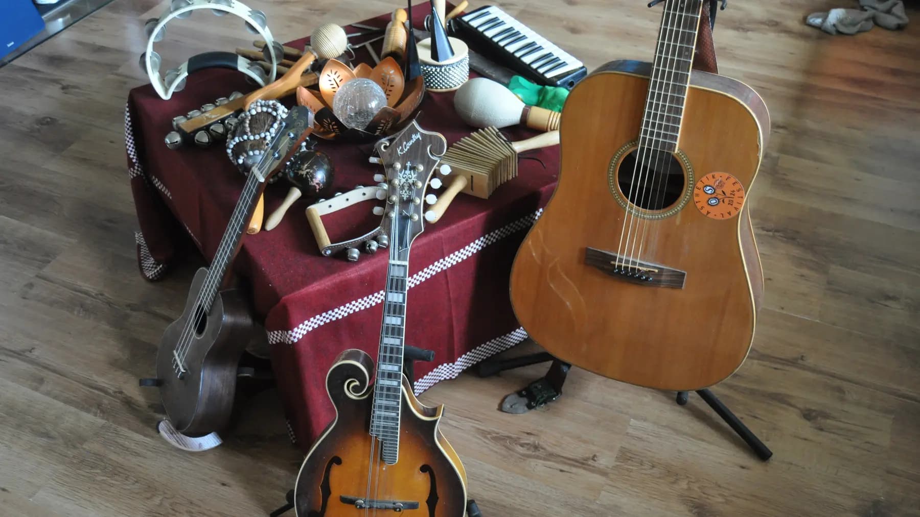 Die Instrumente von Hans Hermsen: eine Westerngitarre auf dem Ständer, davor Mandoline und Ukulele, dahinter ein Tisch mit Percussionsinstrumenten