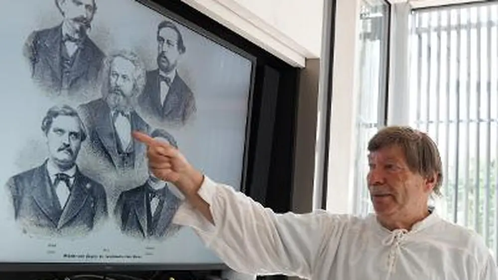 Hans Hermsen bei einem Vortrag: Er zeigt auf eine Bildtafel mit Porträts aus dem 19. Jahrhundert