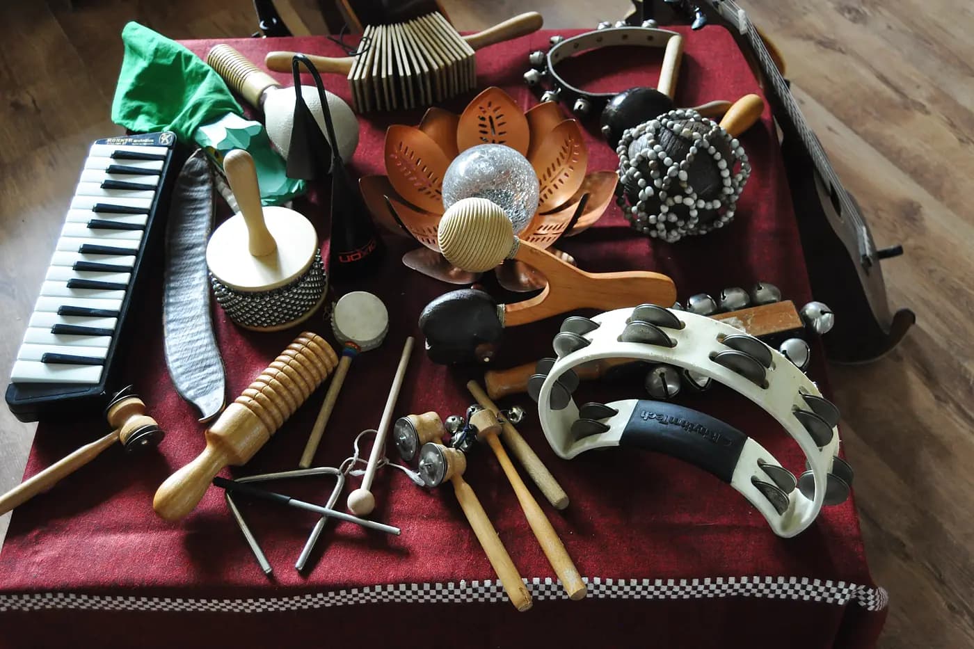 Nahaufnahme der Percussionsinstrumente: Melodica, Schellentrommel, Triangel, Guiro, Klanghölzer und Schellenkränze auf dem roten Tuch