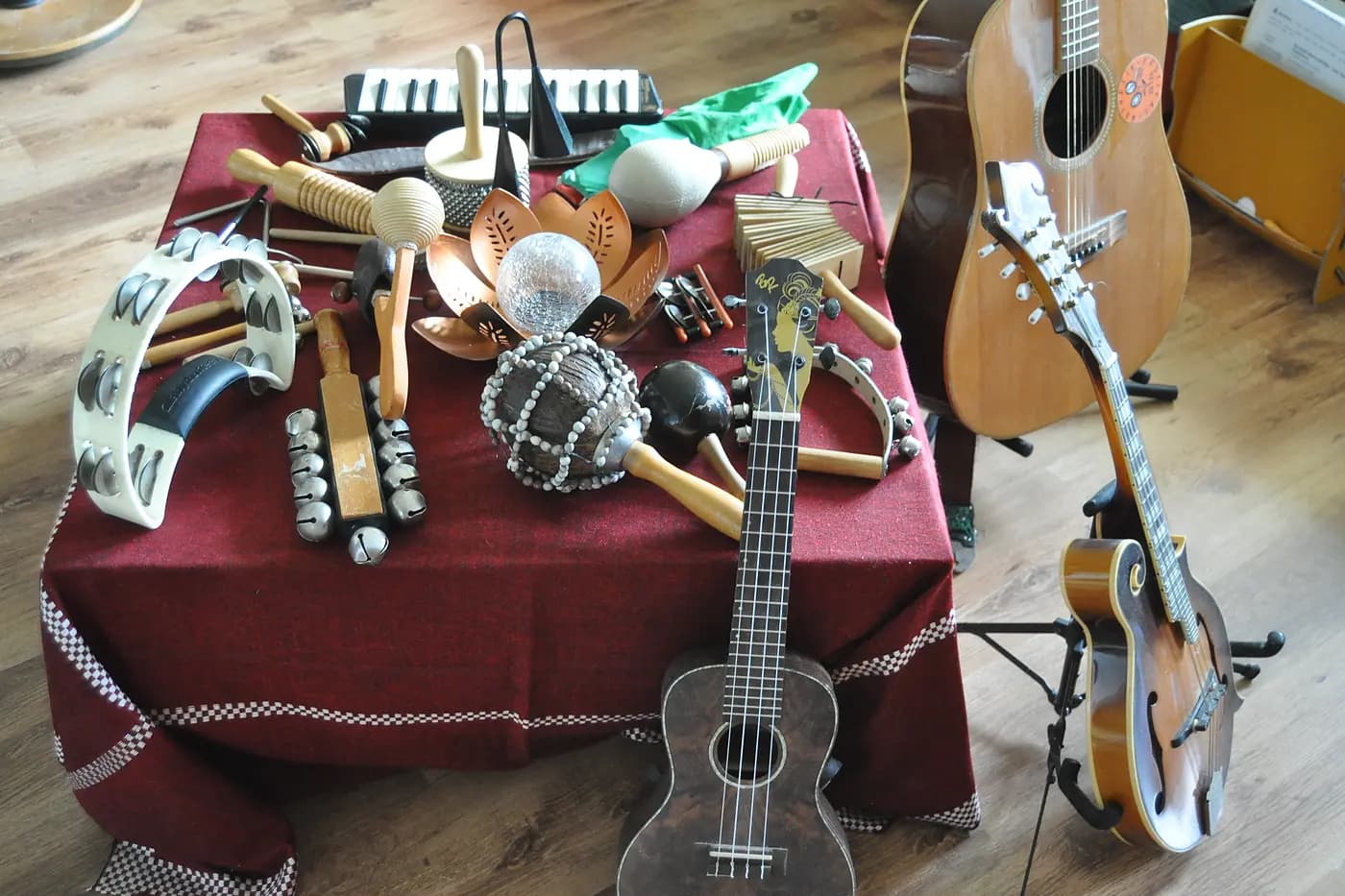 Der gedeckte Instrumententisch von oben: Tamburin, Rasseln, Klanghölzer und Melodica, davor eine Ukulele, rechts Gitarre und Mandoline auf Ständern