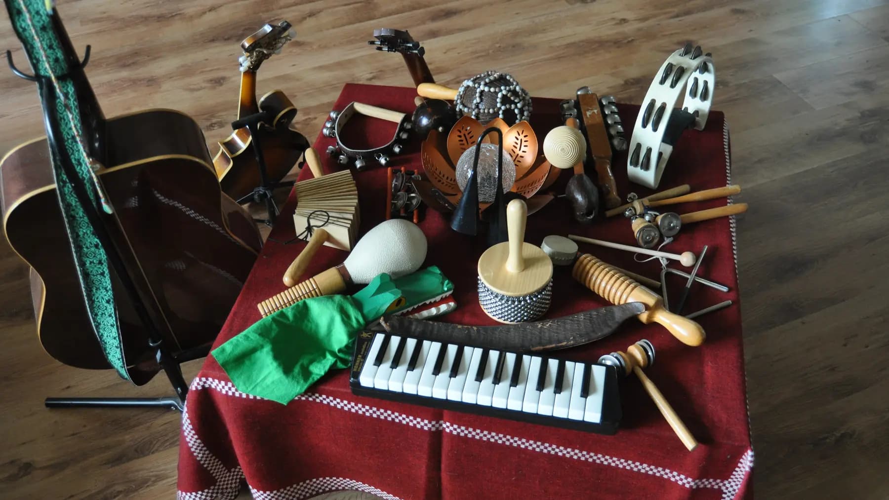 Ein Tisch voller Percussionsinstrumente, daneben Gitarre und Geige auf Ständern: Melodica, Rasseln, Klanghölzer, Tamburin und Schellenkränze