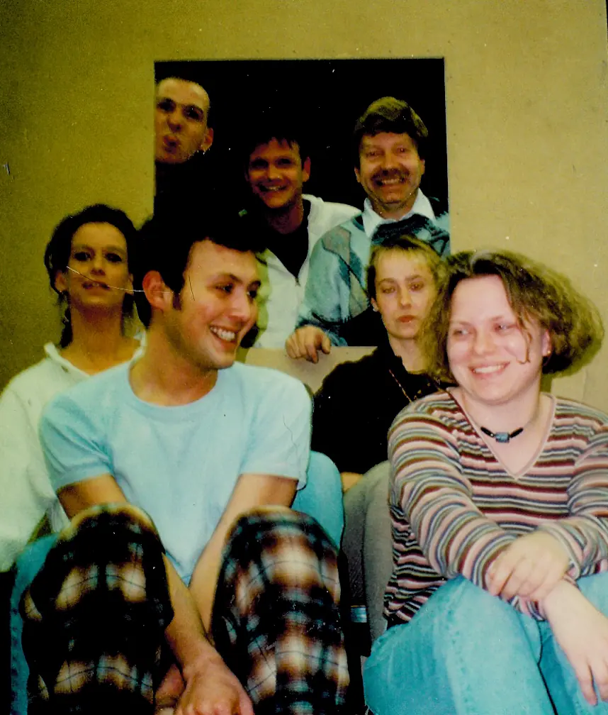 Gruppenbild der Theatergruppe: sieben junge Leute sitzen dicht beieinander und lachen in die Kamera